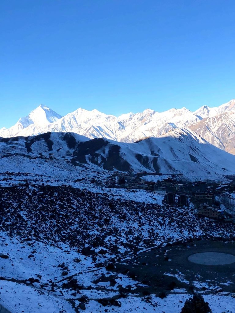 Snow-covered landscape with towering Himalayan peaks under a clear blue sky.