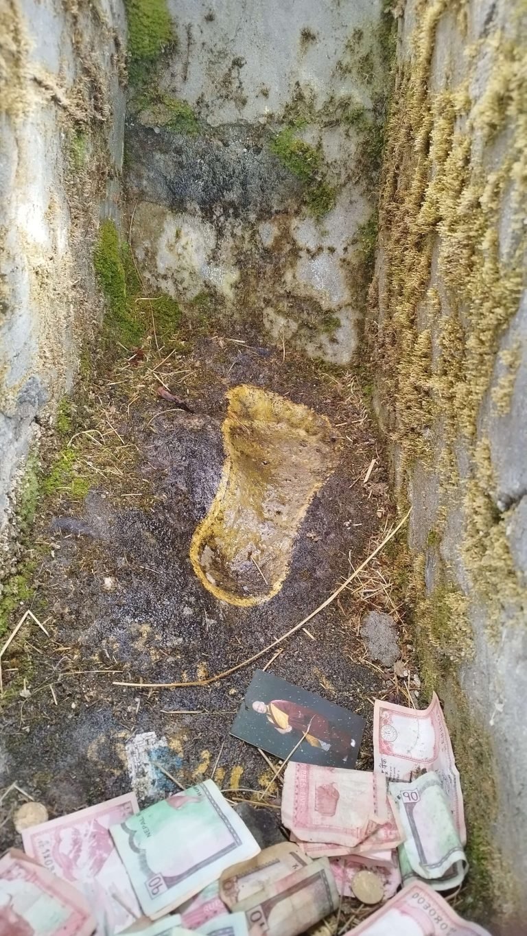 Milarepa's preserved footprint amidst moss and currency offerings in Labchi, Nyalam Valley.