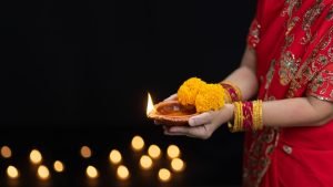 Woman in traditional Nepali attire holding an oil lamp and marigold flowers during Tihar festival