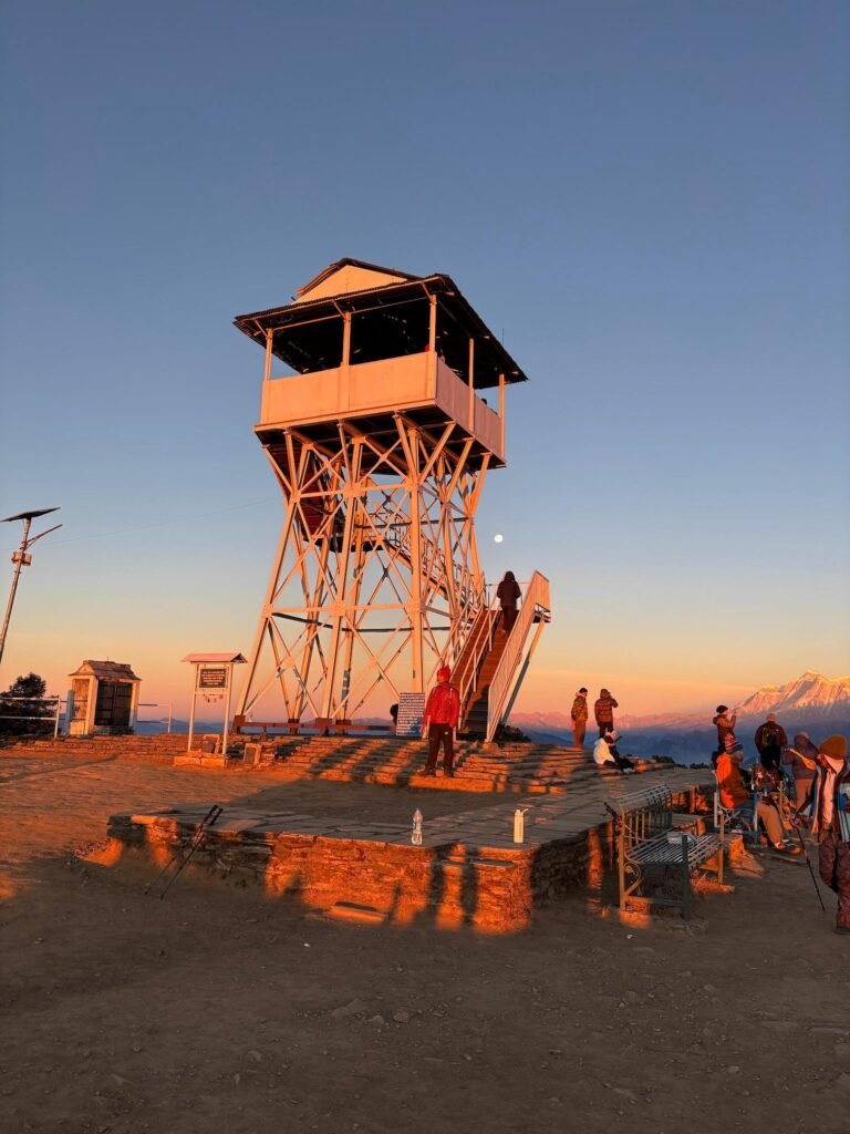 View tower at Poon Hill during sunrise with visitors and distant mountains.