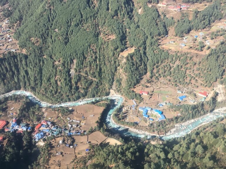 Aerial view of a Nepalese village surrounded by lush greenery, seen from a helicopter during an Everest visit.