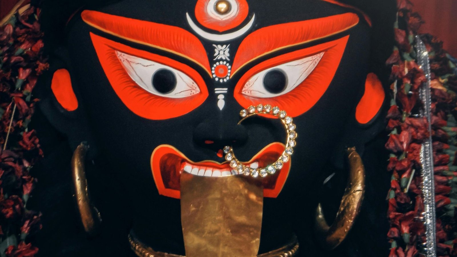 Close-up of Goddess Kali idol with fierce red and black face, wide open eyes, golden nose ring, and protruding tongue.