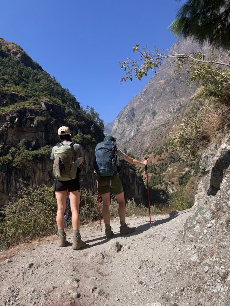 Two hikers with backpacks and trekking poles on a rugged mountain trail near Jagat in Nepal's Manaslu Circuit Trek