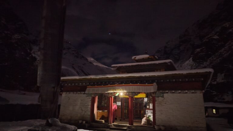 Snowy Lapchi Gumba monastery lit from within at night under towering Himalayan peaks