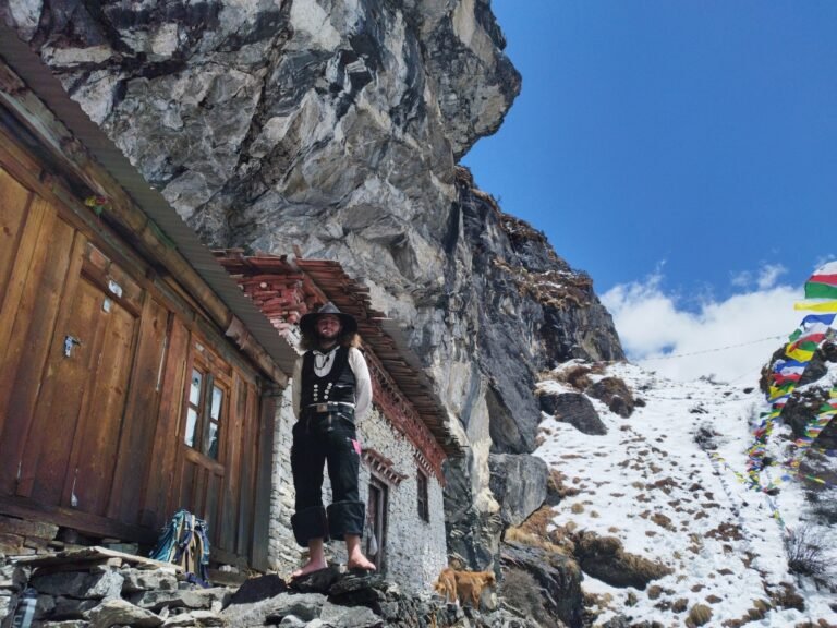 Barefoot trekker at rustic Himalayan cave lodge near Lapchi Shefuk, Nepal with prayer flags and snowy slopes