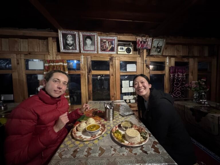 Two trekkers enjoying dinner inside a wooden tea house on the Manaslu Circuit in Nepal