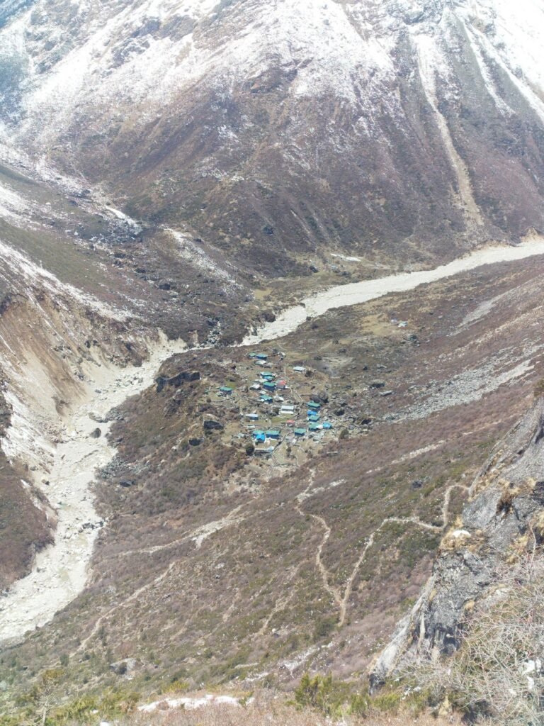 Remote Lapchi Valley in Nepal with steep Himalayan slopes, winding riverbed and cluster of blue-roofed mountain lodges