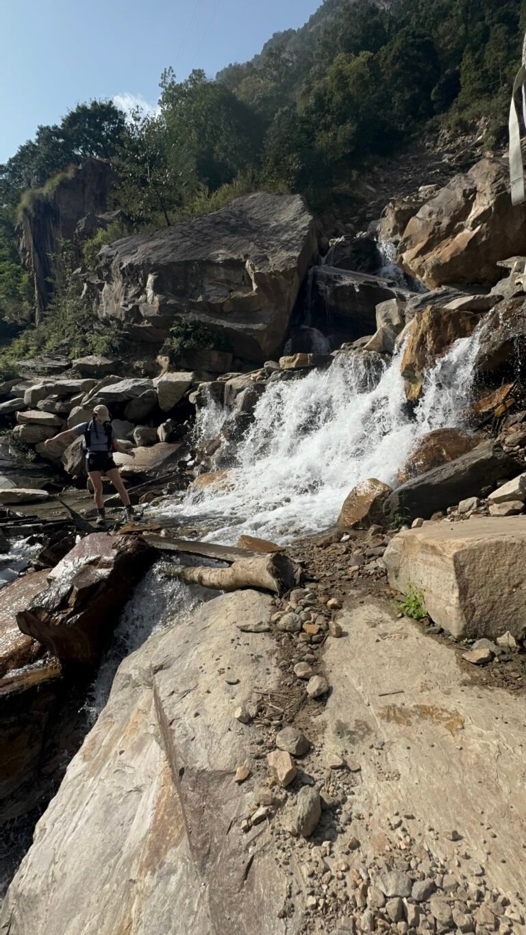 Hiker crossing a rocky stream waterfall at the start of the Manaslu Circuit trek in Nepal