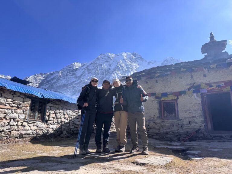 Four trekkers pose in front of Pungyen Gumba monastery with prayer flags and snowy Manaslu peaks in Nepal.