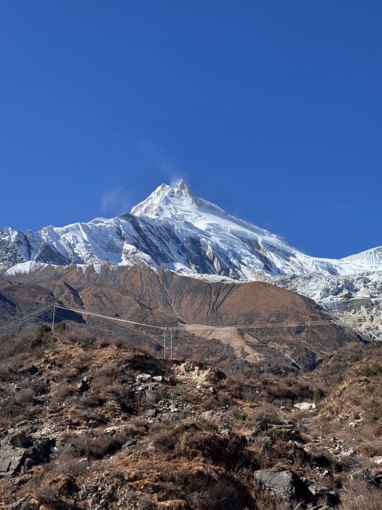 Snow-capped Manaslu peak rising above rugged Himalayan slopes under a clear blue sky on the way to Samagaun