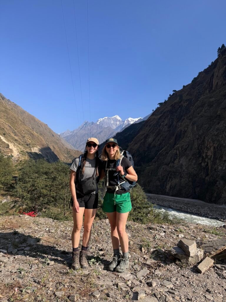Two trekkers on the way to Filim village in Nepal with river valley and snow-capped Manaslu peaks behind