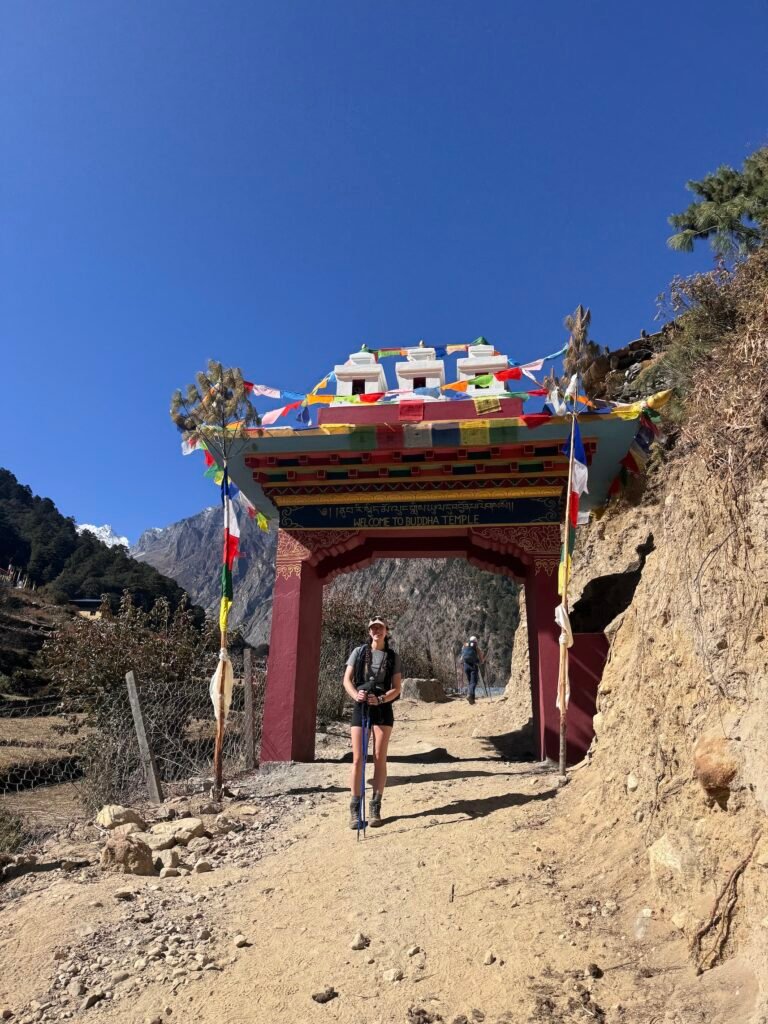 Hiker passing beneath a prayer flag-decorated gate on the way to Lho during the Manaslu Circuit Trek in Nepal