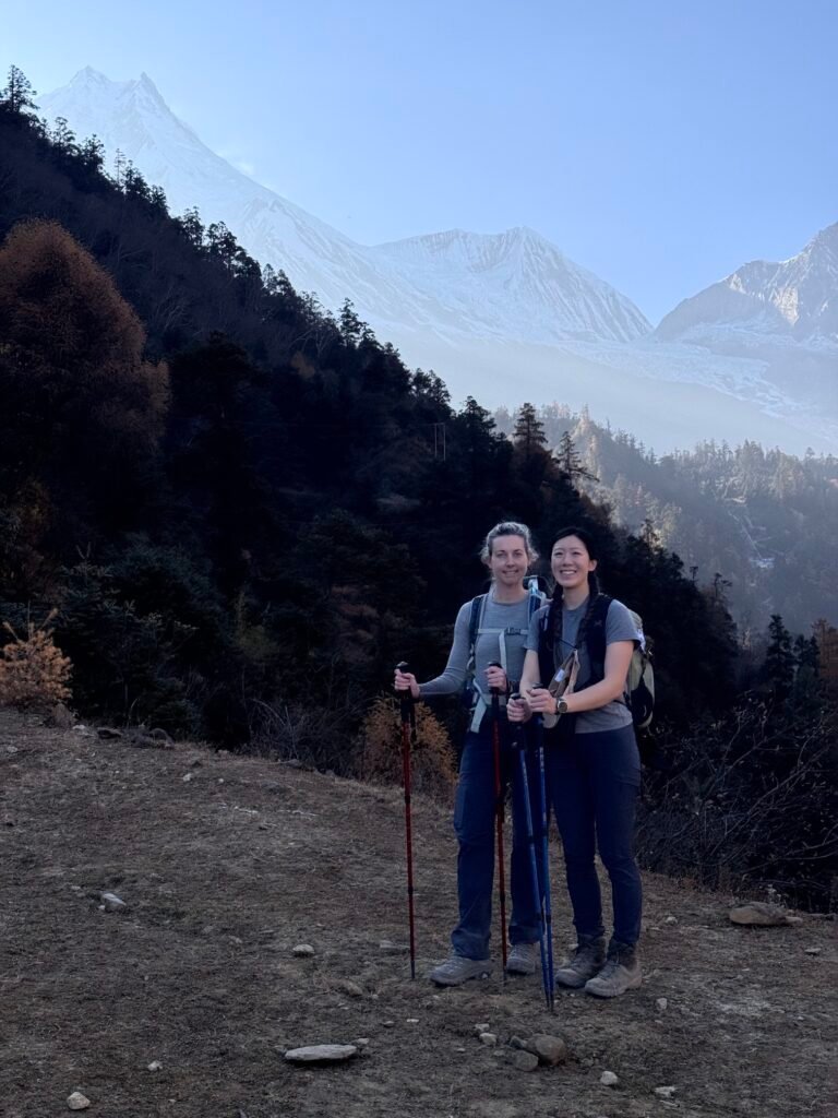 Two trekkers on Pungin Gumba path in Nepal with snow-capped Manaslu peaks behind them