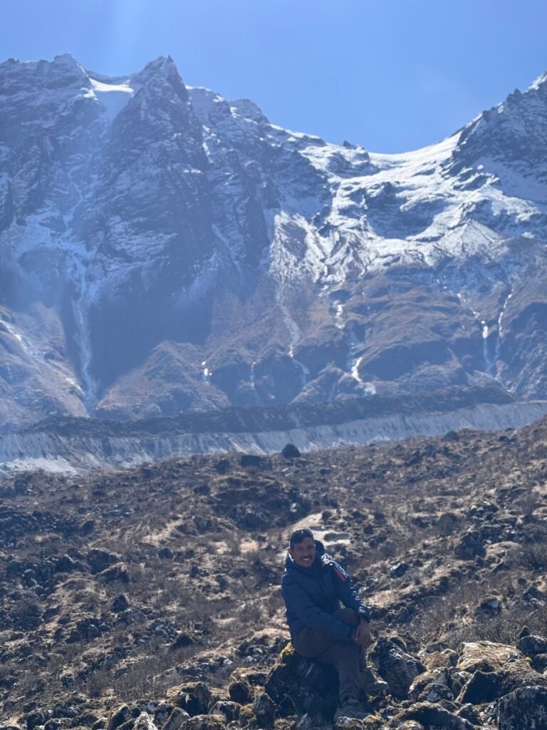 Trekker sitting on a rocky slope with snow-capped peaks behind at Pungin Gumba, Manaslu Circuit Trek, Nepal
