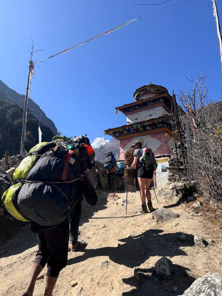Trekkers and a porter carrying heavy loads past a decorated stupa on the Manaslu Circuit trail in Nepal