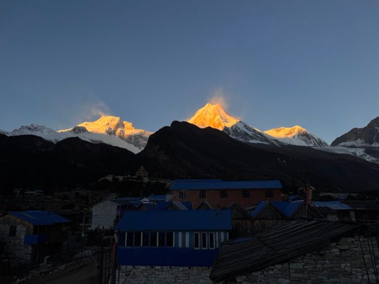 Sunrise illuminating snowy Manaslu peaks above Samdo village with blue-roofed lodges