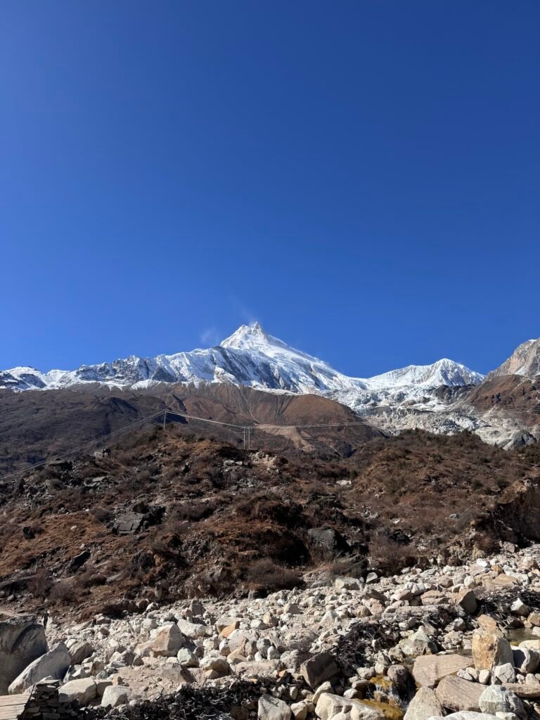 Snow-capped Mount Manaslu towering over rocky slopes at Samagaun village under a clear blue sky