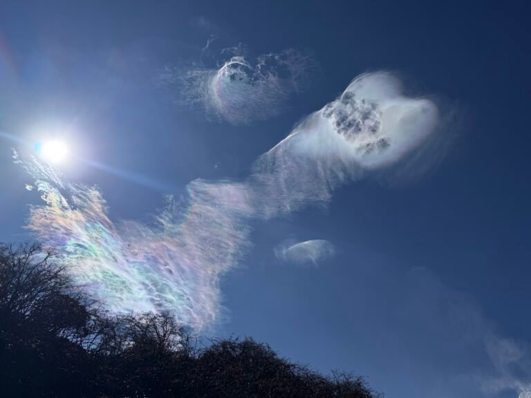 Iridescent clouds shimmering above a mountain ridge under a bright sun on the Manaslu Circuit Trek